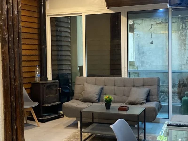 Salon of the Faraya chalet with wood-clad walls, a wood-burning stove and glass doors onto the terrace